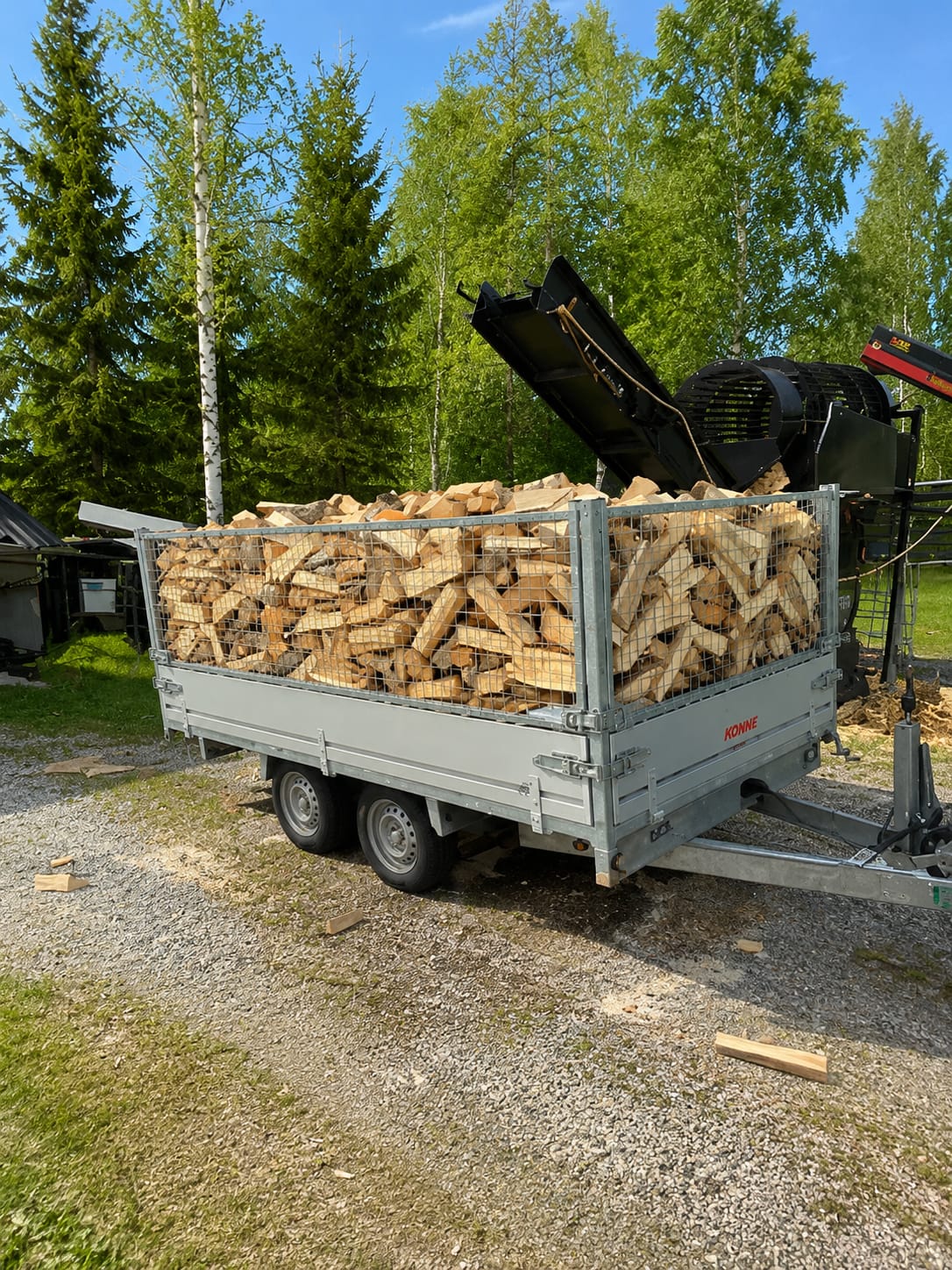 Peräkärry täynnä tuoretta koneellisesti puhdistettua koivuklapia klapikoneen vieressä